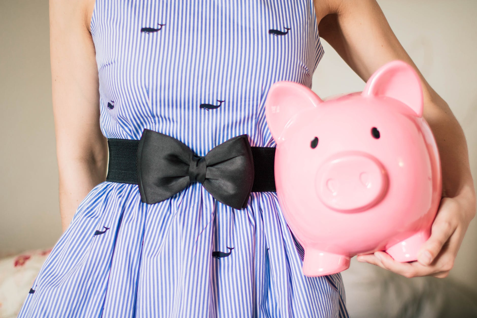 A woman in a blue dress holding a large piggy bank for saving money.