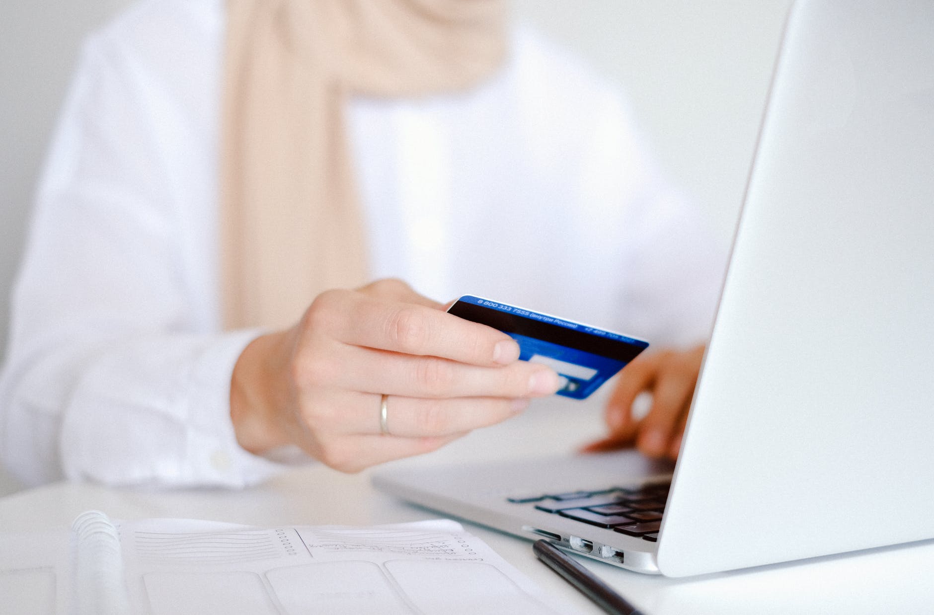 A woman in a white shirt about to make a payment with a debit card on her laptop.