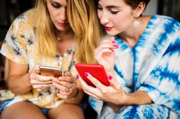 Two girls looking at their mobile phones, one helping the other