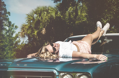 A girl lying down on top of a car in the sunshine