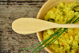 A wooden bowl of cooked rice with a wooden spoon on top of it